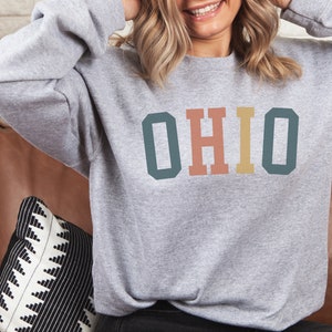 May include: A gray sweatshirt with the word "OHIO" printed in colorful block letters. The letters are in shades of teal, pink, and yellow.