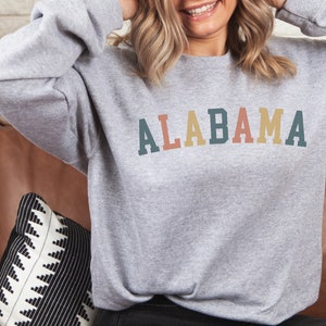 May include: A gray sweatshirt with the word "ALABAMA" printed on the front in colorful letters. The letters are in shades of teal, red, yellow, and orange.