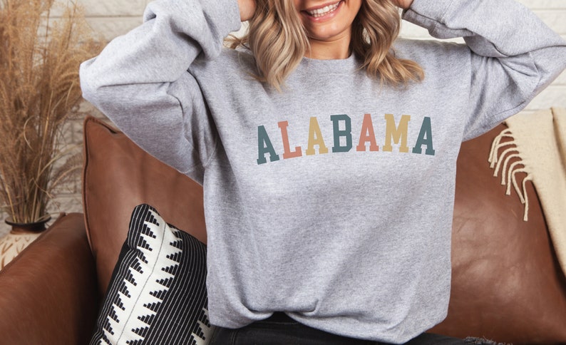 May include: A gray sweatshirt with the word "ALABAMA" printed on the front in colorful letters. The letters are in shades of teal, red, yellow, and orange.