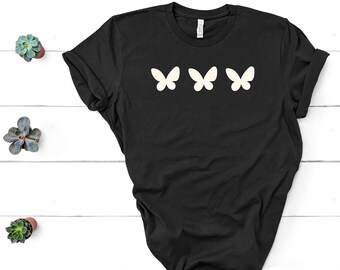Op de afbeelding: Een zwart t-shirt met korte mouwen en een grafische print van drie crèmekleurige vlinders die in een horizontale rij op de borst zijn geplaatst. Het kledingstuk heeft een ronde hals en een standaard pasvorm met een eenvoudig ontwerp.