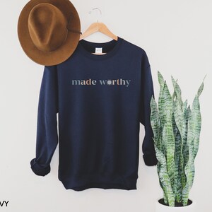 May include: Navy blue sweatshirt with the text "made worthy" in a colorful font with a sun graphic.