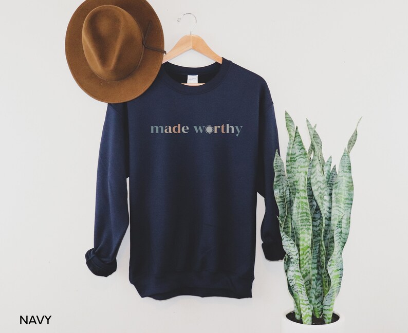 May include: Navy blue sweatshirt with the text "made worthy" in a colorful font with a sun graphic.