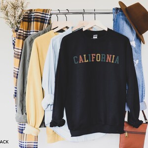 Puede incluir: Sudadera negra con la palabra "CALIFORNIA" impresa en letras de colores en la parte delantera.