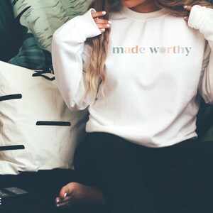 May include: White long-sleeve sweatshirt with the text "made worthy" in pastel colors.