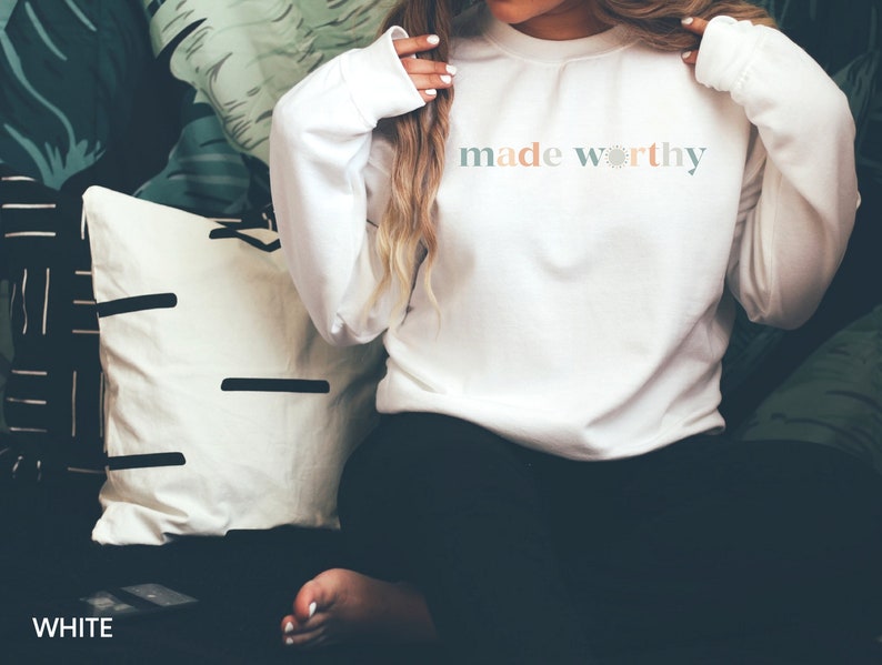 May include: White long-sleeve sweatshirt with the text "made worthy" in pastel colors.
