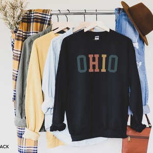 May include: Black sweatshirt with a retro-style graphic of the word "OHIO" in green, orange, and brown.