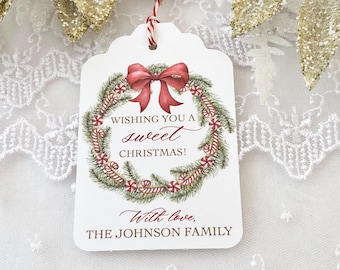 May include: White gift tag with a red bow and a green wreath with candy canes. The text reads "Wishing you a sweet Christmas!" and "With love, The Johnson Family."