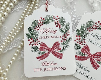 May include: A white rectangular gift tag with scalloped edges featuring a watercolor illustration of a pine wreath with red berries and a red and white checkered bow. The text reads Merry CHRISTMAS! With love, THE JOHNSONS in red and black.