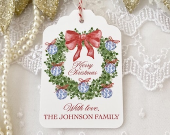 May include: White gift tag with a watercolor illustration of a Christmas wreath with red bow and blue and white ornaments. The text "Merry Christmas" is written in red cursive. The text "With love, THE JOHNSON FAMILY" is written in red cursive at the bottom of the tag.