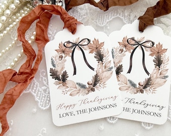 May include: Two white rectangular gift tags with scalloped edges, featuring a watercolor autumn wreath illustration with brown leaves, acorns, and a black bow. The text reads Happy Thanksgiving and LOVE, THE JOHNSONS in black and brown script.