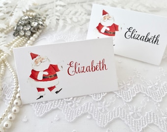 May include: Two white place cards with a watercolor illustration of Santa Claus. The name "Elizabeth" is written in red on one card and black on the other.