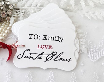 May include: White gift tag with red string and bow. The tag has the text "TO: Emily LOVE: Santa Claus" written on it.