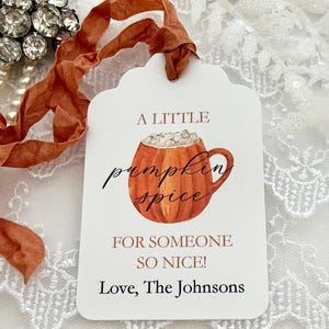 Könnte beinhalten: Ein weißes, rechteckiges Geschenkanhänger-Etikett mit gewelltem Rand und einer Aquarellillustration einer kürbisförmigen Tasse mit einem Getränk. Der Text lautet A LITTLE pumpkin spice FOR SOMEONE SO NICE! Love, The Johnsons. Ein rostfarbenes Band ist befestigt.