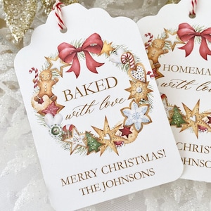 Könnte beinhalten: Weiße Geschenkanhänger mit einem Weihnachtskranz-Design mit Lebkuchen, Zuckerstangen und Sternen. Der Text auf den Anhängern lautet "Baked with love" und "Homemade with love".