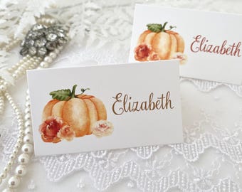 May include: Two white place cards with a watercolor pumpkin and floral design. The name "Elizabeth" is written in brown cursive on each card.