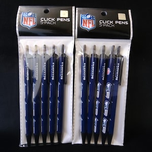 Könnte beinhalten: Zwei 5er-Sets Seattle Seahawks Kugelschreiber. Die Stifte sind marineblau mit dem Teamlogo und dem Wort "SEAHAWKS" aufgedruckt. Die Verpackung enthält das NFL-Logo und die Worte "CLICK PENS 5-PACK".