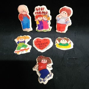 May include: A set of seven Cabbage Patch Kid iron-on patches. The patches feature different designs, including a heart with the text "I love my Cabbage Patch Kid", a patch with two Cabbage Patch Kids and the text "Best Friends", and a patch with a Cabbage Patch Kid on a skateboard.