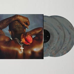 May include: A double vinyl record set with a grey and white marbled design. The album cover features a man with a peach in his hand and the text "Coming Home" in the top right corner.