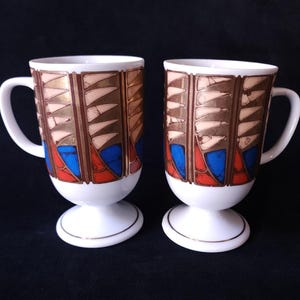 Par de tazas vintage Holt Howard con pedestal, rayas azules, rojas y detalles dorados.