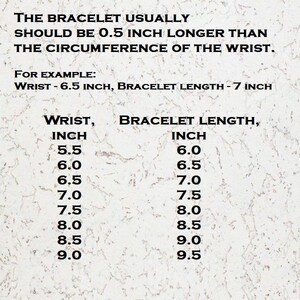 Op de afbeelding: Een maattabel voor armbanden met zwarte tekst op een lichte, gespikkelde achtergrond. Er staat dat de armband 0,5 inch langer moet zijn dan de polsomtrek, met een tabel voor polsmaten van 5,5 tot 9,0 inch en de bijbehorende lengtes.