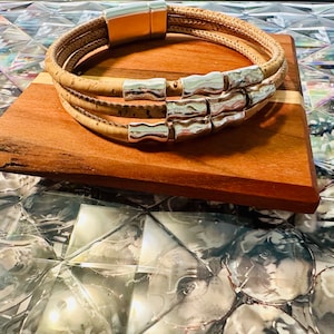 May include: A triple-wrap cork bracelet with silver-toned metal accents. The bracelet has a magnetic clasp.