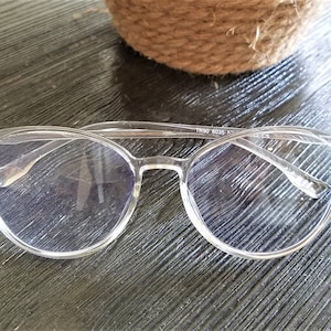 May include: Clear plastic framed glasses with round lenses. The glasses have a subtle blue tint and the text "TM80 8035" is visible on the frame.