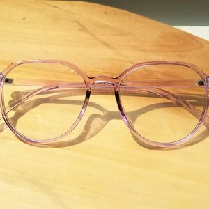May include: A pair of light purple, round, clear-framed glasses with a slightly squared shape.