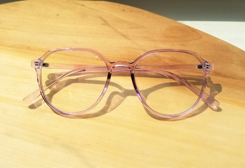 May include: A pair of light purple, round, clear-framed glasses with a slightly squared shape.