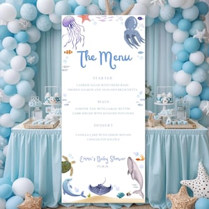 May include: A tall, rectangular menu board with a light blue background, decorated with watercolor illustrations of sea creatures. The menu reads "The Menu" and lists starter, main, and dessert options for a baby shower. The event is for "Emma's Baby Shower" on 03.28.26.