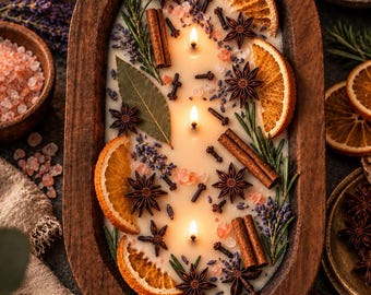 Può includere: Una candela a tre stoppini in una ciotola di legno ovale, riempita di cera bianca e decorata con fette di arancia essiccata, anice stellato, bastoncini di cannella, chiodi di garofano, rametti di rosmarino, lavanda e cristalli di sale rosa.