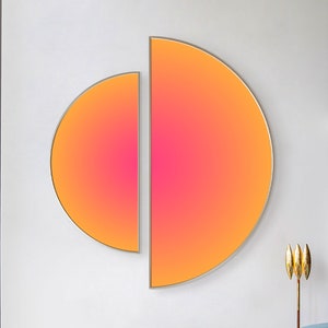 Puede incluir: Una gran pieza de arte mural compuesta por dos paneles semicirculares con un degradado vibrante que transita desde un borde exterior naranja brillante hacia un centro rosa intenso, montada en una pared blanca sobre muebles.