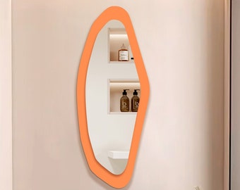 May include: A modern bathroom with a white marble countertop and a rectangular sink. The bathroom features a unique orange-coloured, irregularly shaped mirror hanging on the wall above the sink.