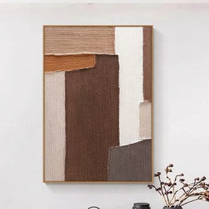 Op de afbeelding: Abstract schilderij met bruine, beige en witte geometrische vormen. Het schilderij is ingelijst en hangt aan een witte muur boven een houten bank.