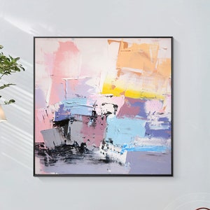 May include: Abstract painting with a mix of pink, purple, blue, yellow, and black paint. The painting has a textured look and is framed in a black frame.