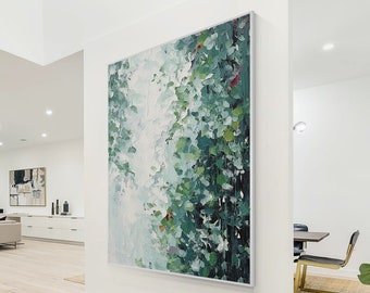 May include: Large abstract painting with a silver frame. The artwork features a blend of green, white, and red brushstrokes, creating a textured, botanical-inspired design. The painting is displayed on a white wall in a modern interior setting.