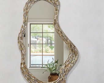 May include: An irregularly shaped mirror with a mosaic-style frame hangs above a white, round sink. The sink sits on a marble countertop with a small, round mirror and toiletries. Two white towels are neatly folded below the countertop.