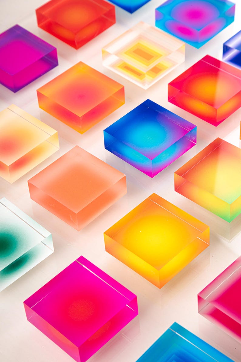 Puede incluir: Una serie de bloques cuadrados transl&uacute;cidos y coloridos en varios tonos de rosa, naranja, amarillo, azul y verde. Los bloques est&aacute;n dispuestos en un patr&oacute;n de cuadr&iacute;cula, creando una exhibici&oacute;n vibrante. Los bloques parecen estar hechos de un material transparente.