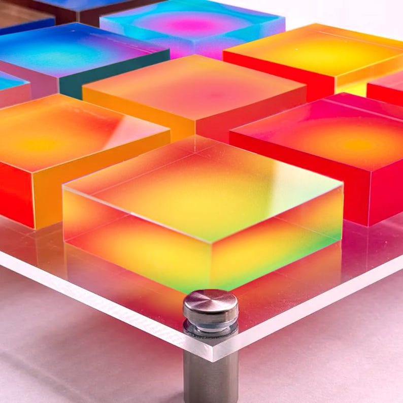 Puede incluir: Una colecci&oacute;n de bloques cuadrados transl&uacute;cidos y coloridos en tonos de azul, rosa, naranja y amarillo. Los bloques est&aacute;n dispuestos sobre una superficie acr&iacute;lica transparente con un soporte met&aacute;lico plateado.