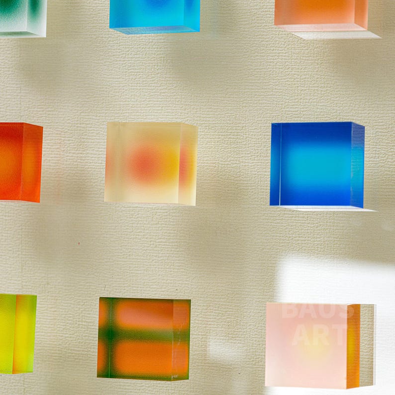 May include: Nine colorful translucent cubes with different color gradients, arranged in a grid pattern on a white wall.