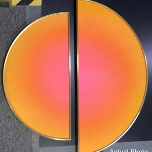May include: Two semicircular wall art pieces featuring a vibrant gradient transitioning from deep orange at the outer edges to a bright pink center. Each piece is encased in a thin, metallic gold frame, creating a cohesive set.