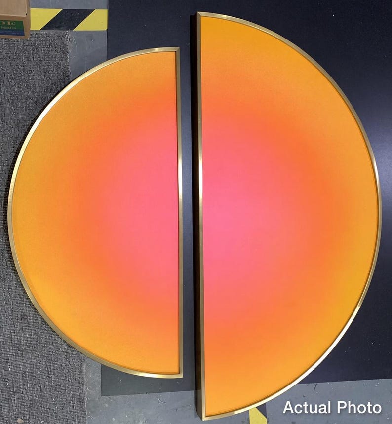 May include: Two semicircular wall art pieces featuring a vibrant gradient transitioning from deep orange at the outer edges to a bright pink center. Each piece is encased in a thin, metallic gold frame, creating a cohesive set.
