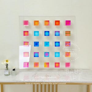May include: A clear acrylic wall art piece with a grid of 18 colorful squares. Each square has a different gradient of color, including pink, orange, yellow, blue, and green. The squares are arranged in a grid pattern, and the piece is mounted on a white wall. The text "ORIGINAL HAND PAINTING 2024" is printed on the piece.