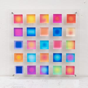 Puede incluir: Una colorida obra de arte mural que presenta una cuadr&iacute;cula de 25 bloques cuadrados. Cada bloque muestra un degradado de colores, incluyendo rosa, amarillo, azul y naranja. La obra est&aacute; montada sobre un panel acr&iacute;lico transparente, creando una est&eacute;tica moderna y vibrante.