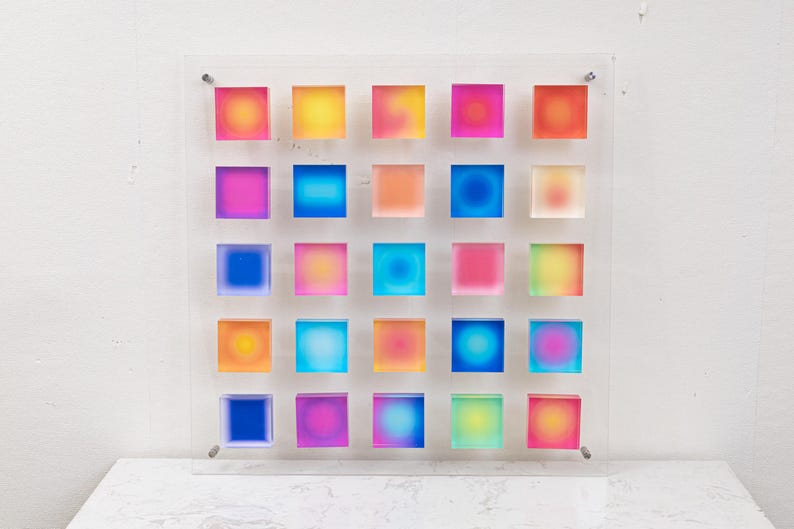 Puede incluir: Una colorida obra de arte mural que presenta una cuadr&iacute;cula de 25 bloques cuadrados. Cada bloque muestra un degradado de colores, incluyendo rosa, amarillo, azul y naranja. La obra est&aacute; montada sobre un panel acr&iacute;lico transparente, creando una est&eacute;tica moderna y vibrante.