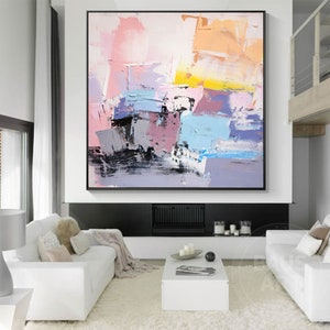 May include: Abstract painting with a mix of pink, blue, yellow, and gray colors. The painting has a textured look and is framed in black.