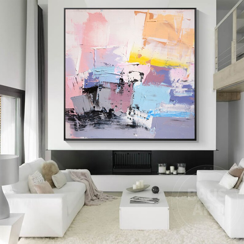 May include: Abstract painting with a mix of pink, blue, yellow, and gray colors. The painting has a textured look and is framed in black.