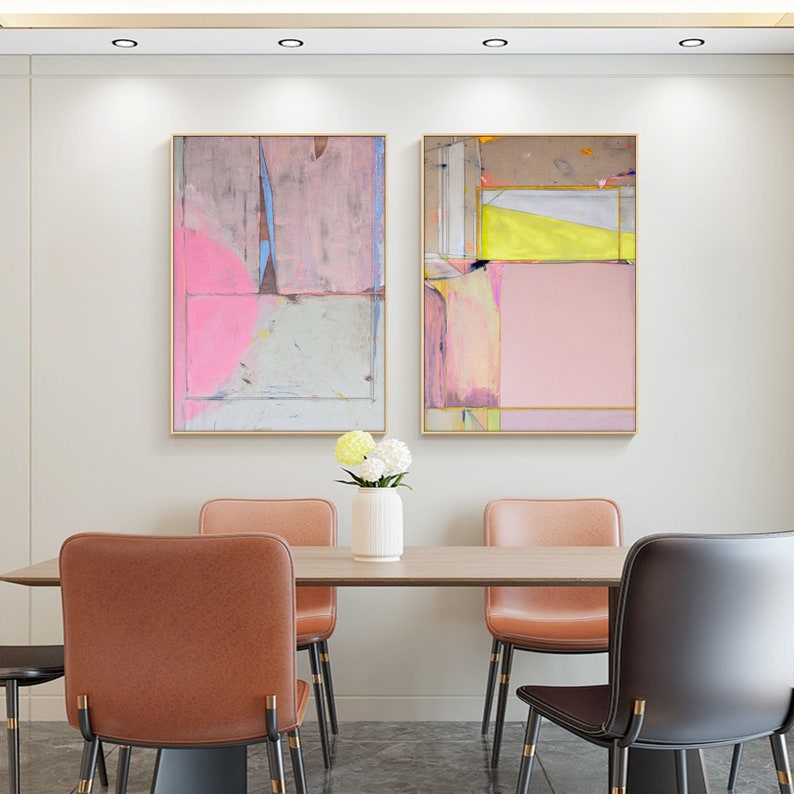 May include: Two abstract paintings with gold frames hang above a dining table. The artwork features pink, yellow, and blue hues. The dining set includes a wooden table, leather chairs, and a white vase with flowers.