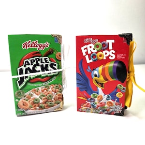 May include: Two small cereal boxes, one green with "Kellogg's Apple Jacks" and the other red with "Kellogg's Froot Loops". Both boxes are tied with string and have gold corner protectors.