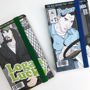 May include: Two small, paperback comic books with elastic bands. The book on the left features a man with a beard and the text "You have a date with the one arm tener..." and "Logan Lucky". The book on the right features a man driving a bus and the text "The bus driving poet from Paterson, NJ." and "Paterno".