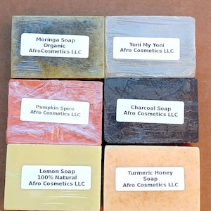 Könnte beinhalten: Sechs handgemachte Seifen mit verschiedenen Düften und Zutaten. Die Seifen sind in Klarsichtfolie verpackt und mit dem Namen der Seife und dem Firmennamen Afro Cosmetics LLC beschriftet. Die Seifen sind in zwei Reihen zu je drei angeordnet.